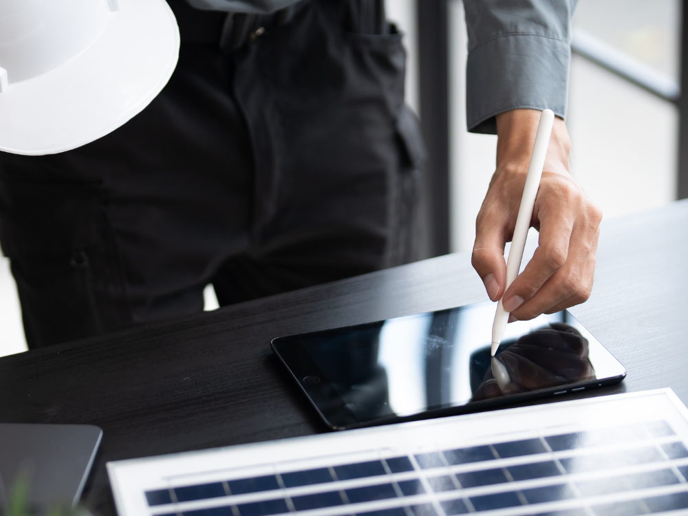 Engineer with a hard hat working on a tablet beside a solar module — representative image